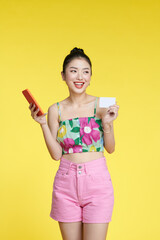 Attractive stylish woman showing credit card and smartphone, smiling on yellow