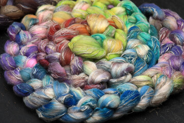 Fototapeta na wymiar Colorful, handdyed roving of sheepwool, braid and rolled up, natural material ready for spinning on a traditional spinning wheel as a hobby.
