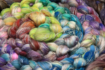 Fototapeta na wymiar Colorful, handdyed roving of sheepwool, braid and rolled up, natural material ready for spinning on a traditional spinning wheel as a hobby.