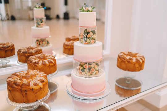 White wedding cake decorated by flowers standing on festive table with lots of snacks on side. Violet flowers on foreground. Wedding. Recetion