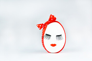 Minimal Easter or cosmetic salon concept. White Easter egg with eyelashes and cute in a coquettish red polka-dot headband on a white background, Self care.
