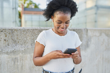 Happy woman using smartphone chatting online in city listen to music on wired earphones