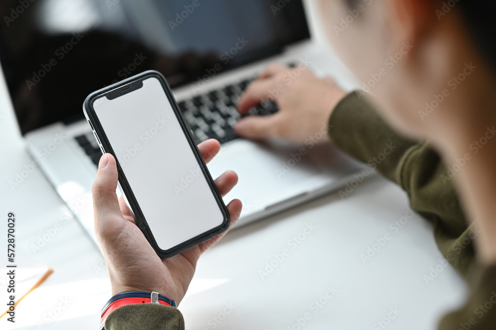 Poster close up and cropped image of young asian man using smartphone while working with laptop, empty scre