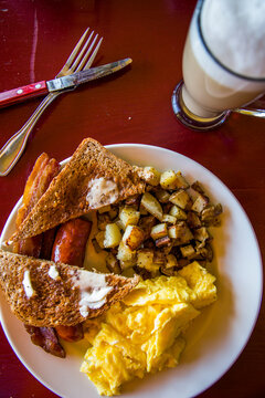 A plate of breakfast food including toast, bacon, potatoes and eggs with a latte on the side at a restaurant in California.