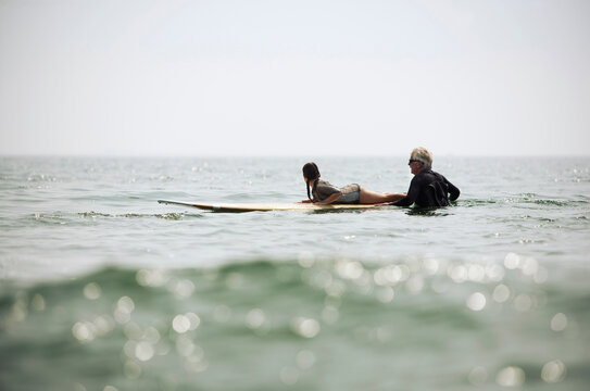A grandfather helps a young girl learn to surf