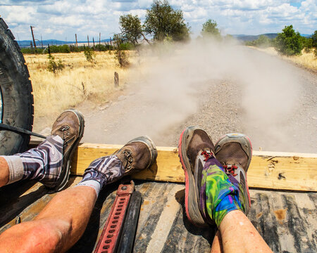 Two pair of  legs two thru hikers in the back of a dusty pick up truck.