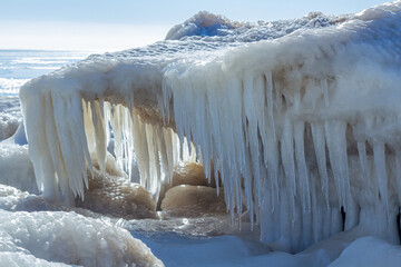 Close-up of the icy seashore, frozen waves, rocks and sun glare on the ice