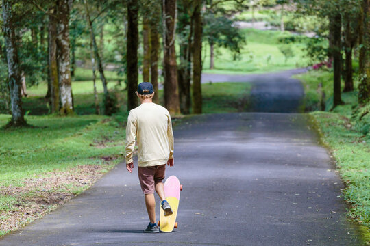 Rear view of man with skateboard walking down street, Bedugul, Bali, Indonesia