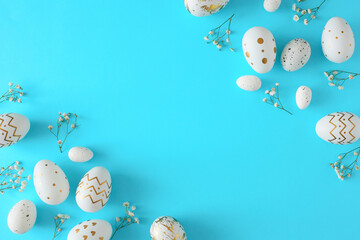 Hello Easter concept. Top view composition of white gold eggs and gypsophila flowers on pastel blue...