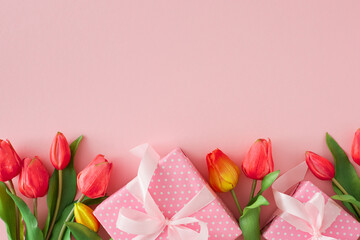 Woman day gift concept. Flat lay photo of present gift boxes and tulips flowers on pastel pink background with empty space. Holiday spring idea.