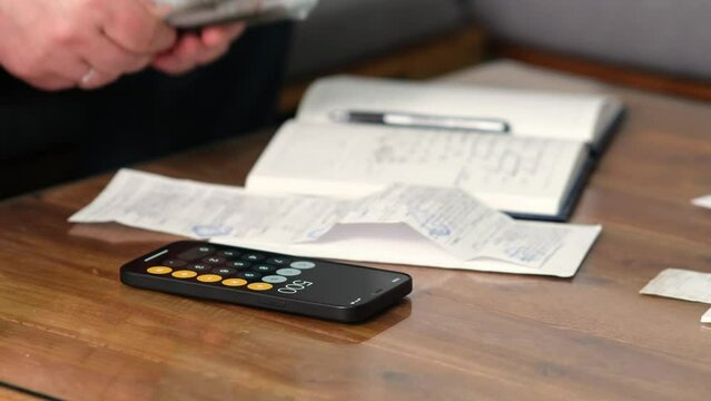 Summary and analysis of expenses and income for goods and services and salary. A person calculates utility bills and receipts using a smartphone calculator. A man counts money in cash dollars, euros.