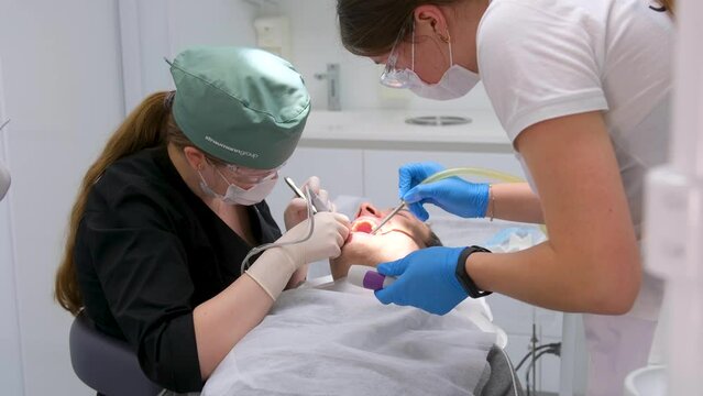 The dentist and his assistant treat the patient. Dental treatment in modern dentistry. A close-up shot of patient in a dental chair undergoing a tooth extraction procedure. Medicine and healthcare 4k