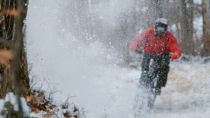 Silhouette of a MTB rider appearing through spraying snow cloud at forest trail