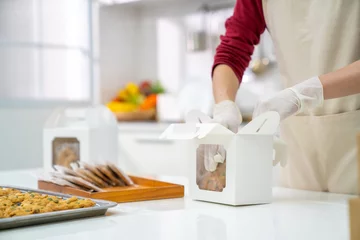 Foto op Plexiglas Asian woman bakery shop owner preparing customer order cookie in delivery box on kitchen counter. Woman bakery chef making bakery in the kitchen. Small business entrepreneur and food delivery concept. © CandyRetriever 