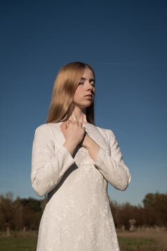 portrait of young woman in white dress praying outside with blue sky