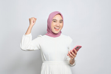 Excited young Asian Muslim woman using mobile phone and celebrating success, getting good news...