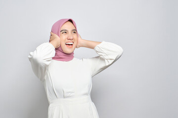 Angry young Asian Muslim woman screaming covering ears with both hands, distressed by noise isolated over white background