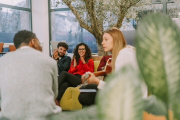 Young people applauding their female colleague while she is playing guitar and singing for them