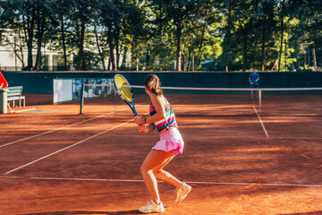Obraz premium View from the back of a young female paying tennis on a court outside