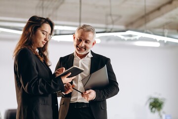 Girl in glasses shows digital tablet to colleague. Two coworkers using gadget in the office