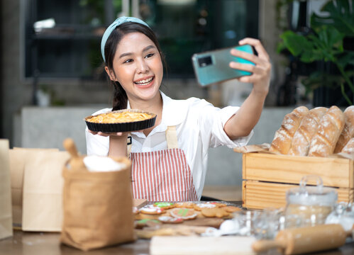 Beautiful Woman Chef Blogger Talking To Smartphone Live Recording Video On Social Network At Home. Asian Online Vlogger Influencer Enjoy Selling Homemade Bakery Pies On Social Media Via Mobile Phone