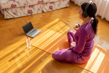 Beautiful woman practicing yoga at home sitting in lotus pose on yoga mat meditating smiling...