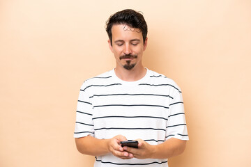 Young caucasian man isolated on beige background sending a message with the mobile