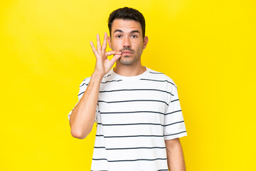 Young handsome man over isolated yellow background showing a sign of silence gesture