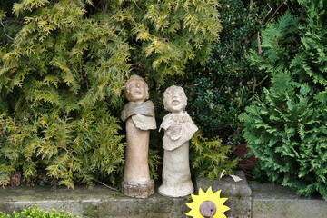 zwei kleine Figuren neben einem Grab unter Koniferen auf einem Friedhof in Velbert