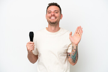 Young caucasian singer man picking up a microphone isolated on white background saluting with hand with happy expression