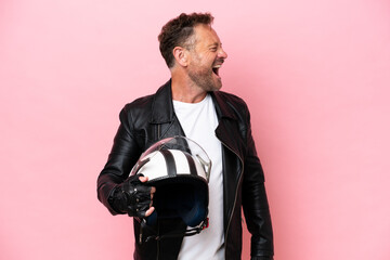 Middle age caucasian man with a motorcycle helmet isolated on pink background laughing in lateral...