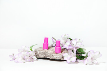 Manicure or pedicure background. Creative mockup of isolated cosmetics bottles with pink and green nail polish with plant, on stone, on white background with hard shadows from plants.