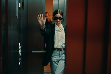 Stylish woman in black jacket and sunglasses posing in elevator, fashion model, dark cinematic light and color, glamor vintage