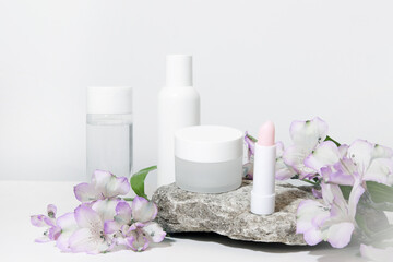 Fototapeta na wymiar White cosmetics background. Cosmetic bottle containers with flowers plant . Blank label package for branding mock-up, with hard shadows. Natural organic beauty product concept.