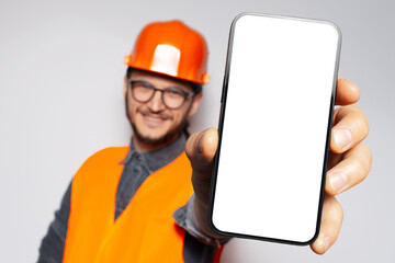 Big smartphone with blank on screen in hand on construction worker, smiling man. Close-up view. Mock up concept. White background.