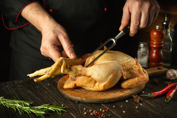 Dish of fried chicken by the hands of the chef in the kitchen of the restaurant. Preparing to cook a raw rooster on a cutting board. Fork in the cook hand.