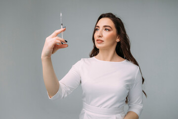 young woman doctor in a white coat holds an insulin syringe in her hand. Girl cosmetologist preparing to make an injection of hyaluronic acid in a cosmetology clinic