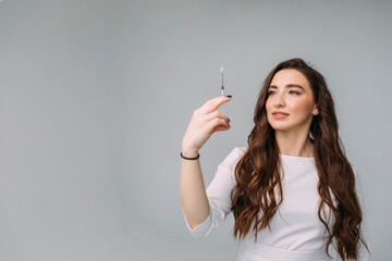 young woman doctor in a white coat holds an insulin syringe in her hand. Girl cosmetologist preparing to make an injection of hyaluronic acid in a cosmetology clinic, copy space