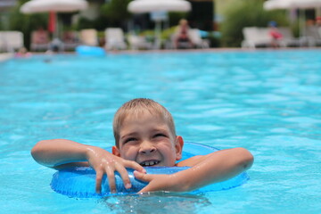 Fototapeta na wymiar Happy little boy swims in the pool in summer, space for text