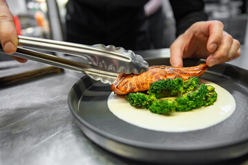 chef hand preparing a gourmet salmon steak with broccoli and salad on restaurant kitchen