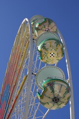 Low angle view of ferris wheel with colorful gondolas and blue sky background.