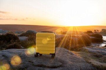 Yellow Suitcase  on top of hill or mountain against blue sky at sunrise. Travel concept.