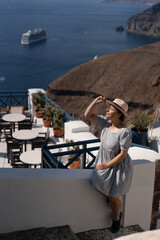 Tourist woman in blue dress with hat relaxing at sea view in the traditional village Thira. Walking Santorini tour, Greece, during her summer  crouise travel. European tourism attraction in Greece