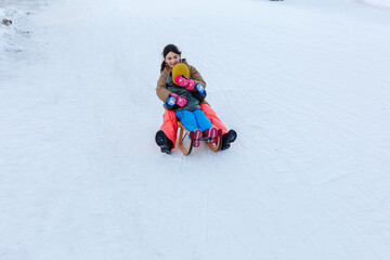 Fototapeta na wymiar two girls sledding on snow slope at wooden sleigh