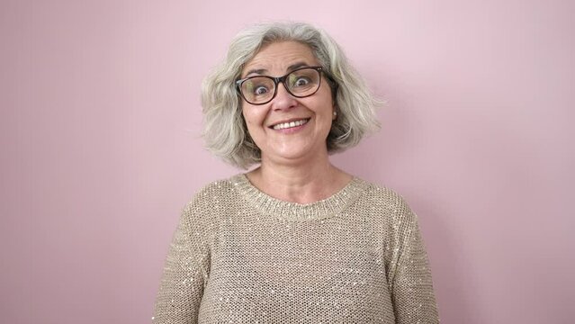 Middle age woman with grey hair smiling confident standing over isolated pink background