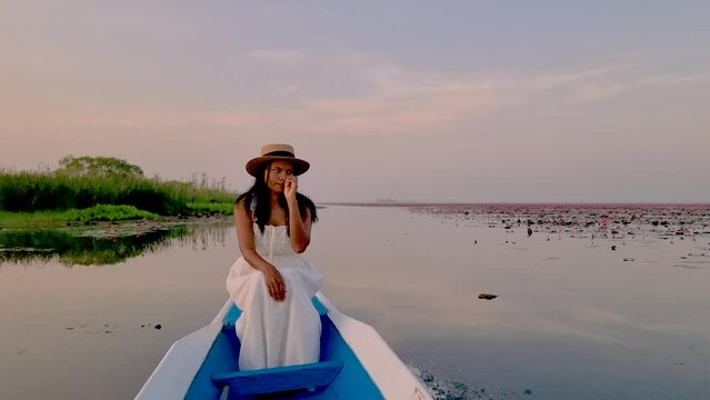 Asian women in a wooden boat during sunrise at the red lotus lake in Thailand , Sunrise at The sea of red lotus, Lake Nong Harn, Udon Thani, Thailand