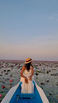 Sunrise at The sea of red lotus, Lake Nong Harn, Udon Thani, Thailand. A Asian women in a wooden boat during sunrise at the red lotus lake in Thailand 