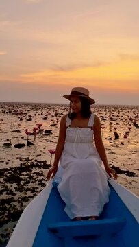 Sunrise at The sea of red lotus, Lake Nong Harn, Udon Thani, Thailand. An Asian woman in a wooden boat during sunrise at the red lotus lake in Thailand 