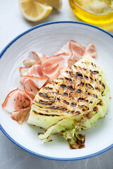 Middle close-up of grilled green cabbage steak with bacon served in a white plate, vertical shot