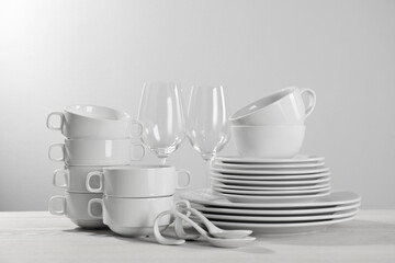 Set of clean dishware and glasses on white wooden table against light background
